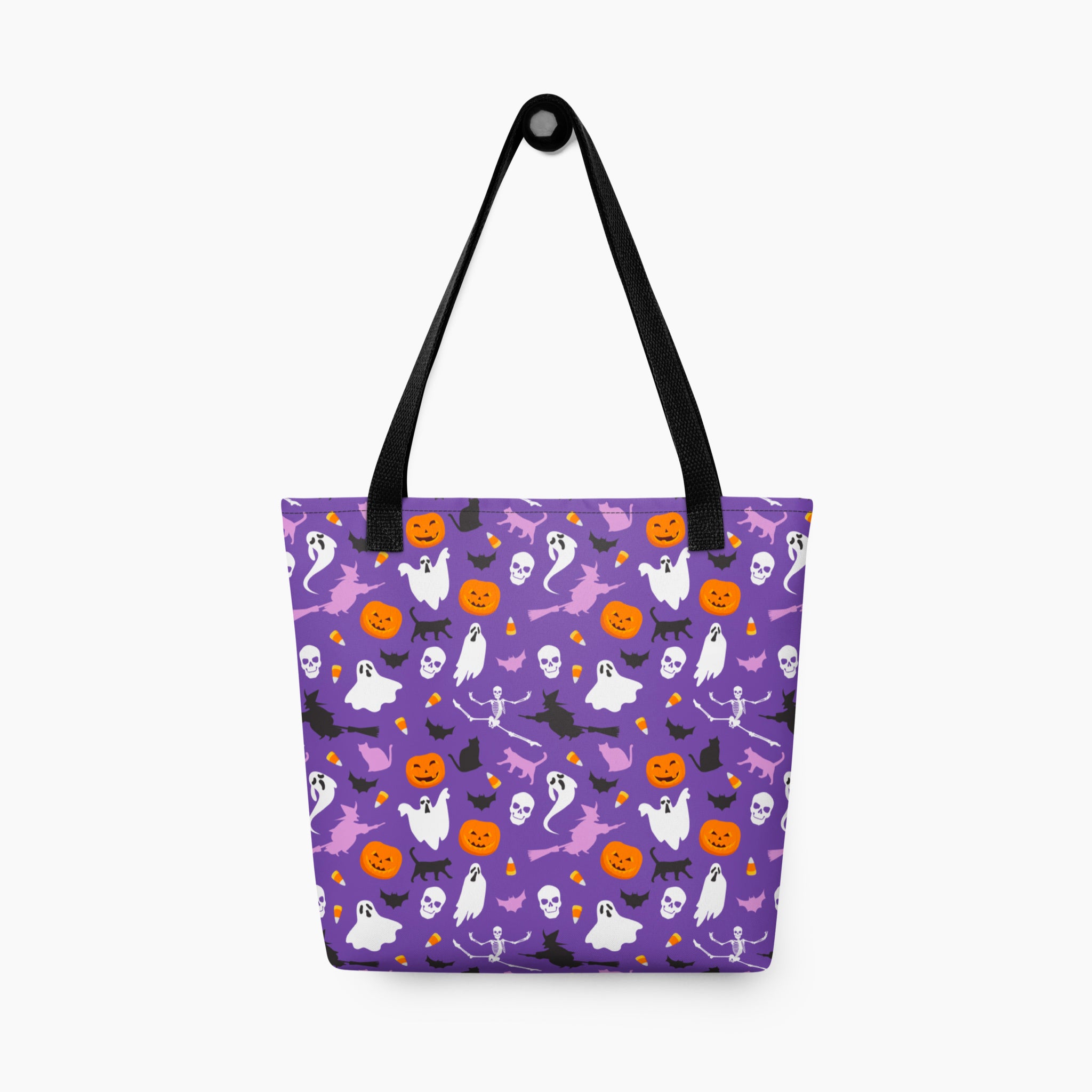 A purple tote bag with a Halloween pattern featuring white ghosts, orange pumpkins, black bats, witch silhouettes, and skulls, complete with black shoulder straps, shown against a plain light grey background.
