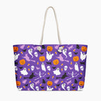 A purple tote bag with a Halloween-themed print featuring ghosts, pumpkins, bats, skeletons, and cats, complete with white rope handles, shown against a plain light-grey background.