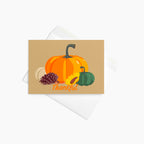 A rectangular autumn-themed greeting card with a tan background and illustrated pumpkins, a pinecone, a sunflower, and the word 'Thankful' in orange script, shown with a white envelope sitting on a light gray background.
