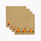 Four tan square cloth napkins layered in a fan arrangement, each printed with a small autumn harvest motif including orange pumpkins, green gourds, pinecones near the bottom.
