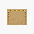 A cloth placemat with a decorative autumn border featuring pumpkins and sunflowers, sitting flat on a light grey background.