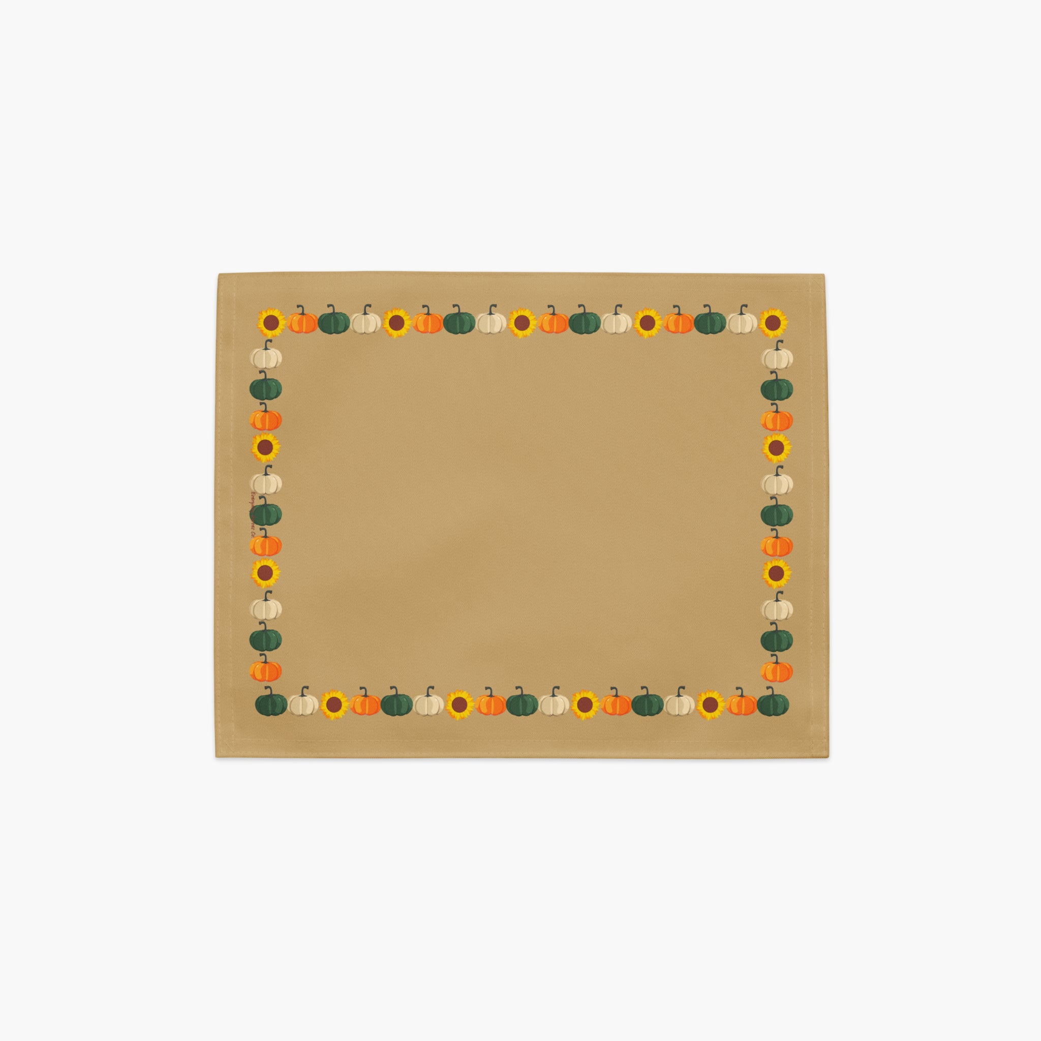 A cloth placemat with a decorative autumn border featuring pumpkins and sunflowers, sitting flat on a light grey background.