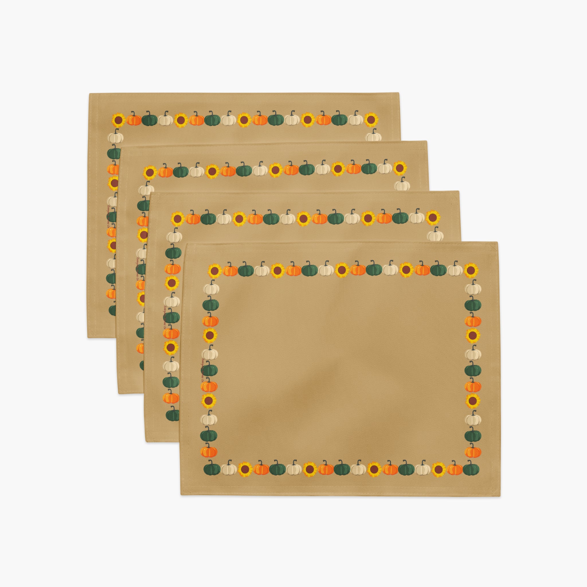 Four tan cloth placemats with a decorative autumn border featuring pumpkins and sunflowers, arranged in a staggered stack on a white background.