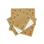 Close-up of four tan cloth placemats with a decorative autumn border featuring pumpkins and sunflowers, arranged in a stack on a light grey background.
