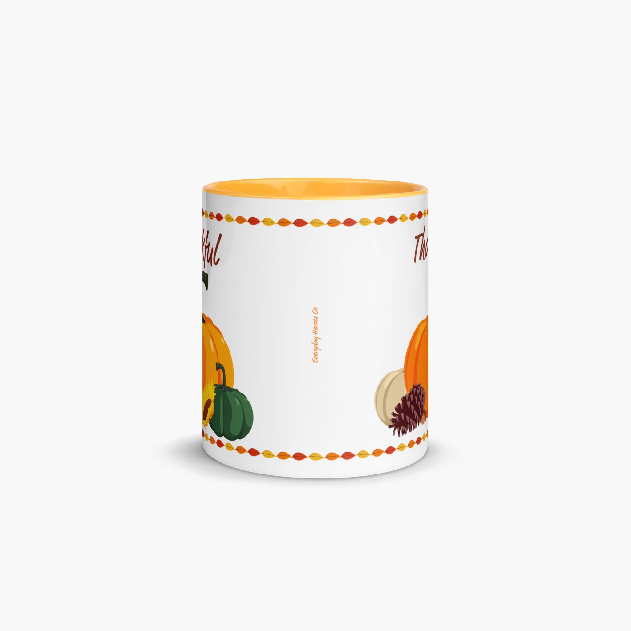 A white ceramic mug with a yellow interior, decorated with autumn-themed illustrations including pumpkins, and a pinecone, framed by a colorful leaf border. The mug is shown on a clean, light gray background.