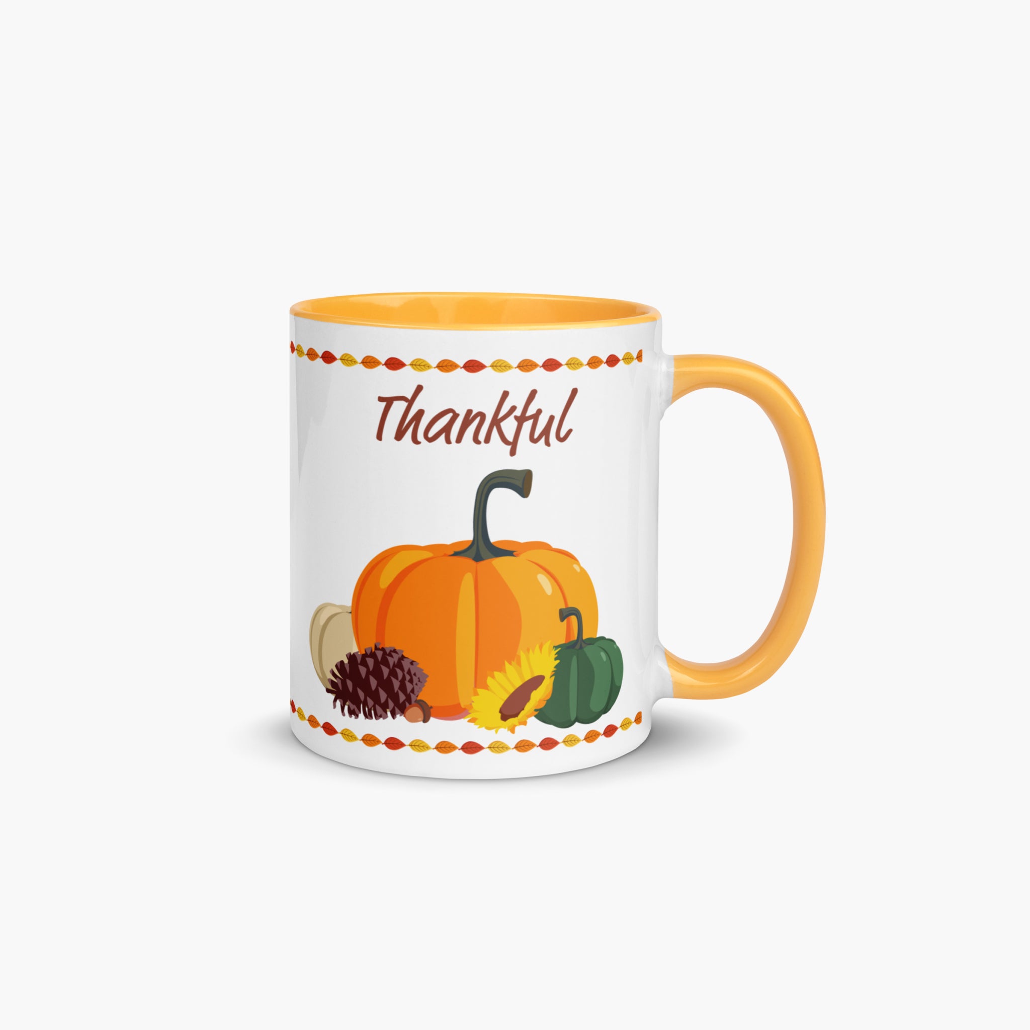 A white ceramic mug with a yellow-orange handle and interior, decorated with a fall harvest theme featuring pumpkins, a pinecone, a sunflower, and the word 'Thankful' in brown script.