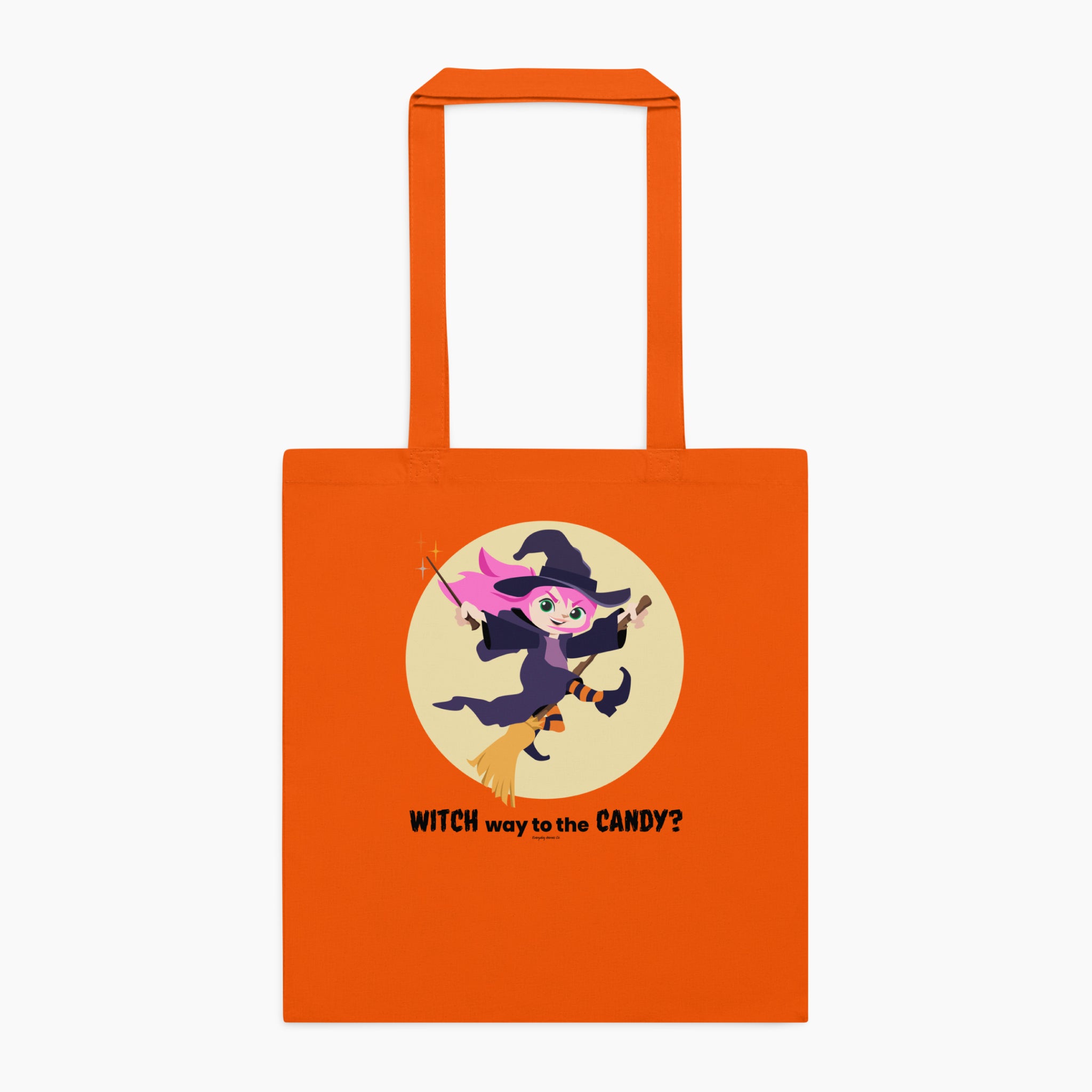 A orange canvas tote bag with orange handles, featuring a 'Witch way to the Candy' message and cartoon girl dressed up as a witch on a broom, set against a plain light grey background.